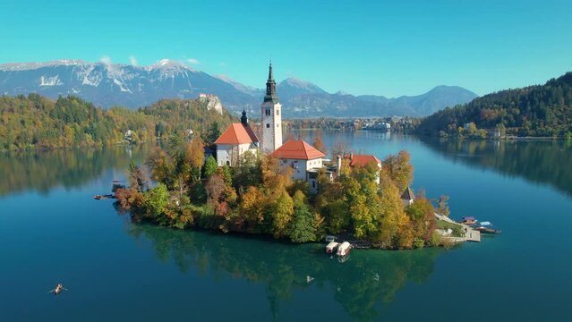 AERIAL: Fairy tale view of little island on lake Bled in colorful autumn shades. Famous Bled island with church in the embrace of vibrant autumn trees. Beautiful fall season creating picturesque views