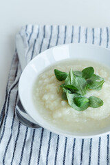 Healthy vegan cauliflower cream soup with herbs in white bowl