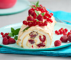 Baked meringue roll with red berries on a round plate, white background