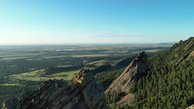 Drone footage flying past the top of the Flatiron rock formations west of Boulder, Colorado on a bright summer morning for an aerial view looking out on the North Colorado plains.