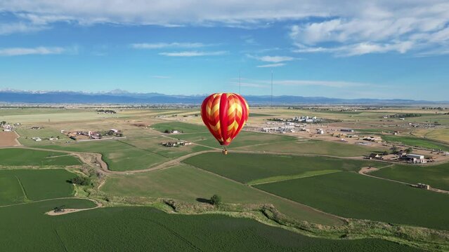 Aerial video of red hot air balloon soaring over great plains farmland in eastern Colorado with mountains in distance