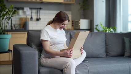 Pregnant beautiful woman received a parcel by courier home, package, gift. He sits on the sofa at home, opens a paper box, rejoices, smiles