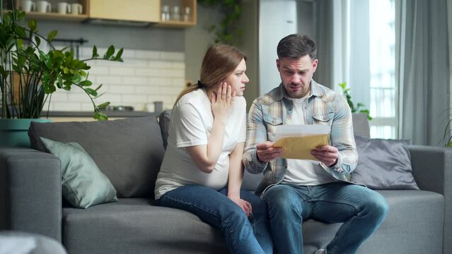 Upset Worried couple, man and pregnant woman at home, open envelope received a letter read with bad news, notice from bank reading loan denied worry with analysis results statement approval