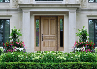Wood grain front door of house surrounded by columns and summer flowers
