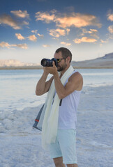 Landscape photographer man taking photographs with digital camera. Travel, vacations, work and active lifestyle concept. Handsome muscular caucasian man using picture with dslr camera on beach