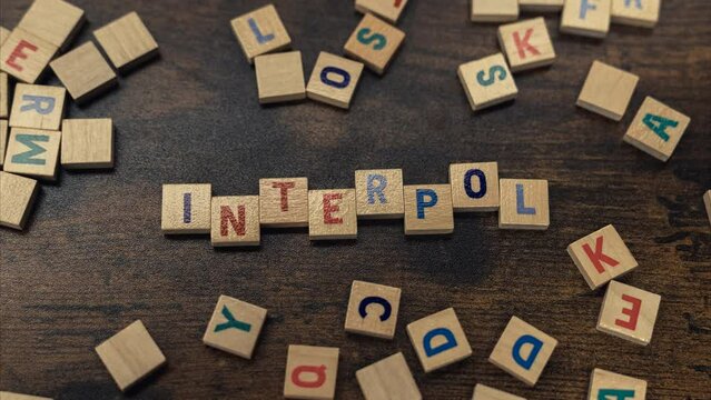 Top view of colorful square wooden letters creating the word INTERPOL. The International Criminal Police Organization concept. High quality 4k footage