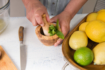 Hands crush mint with a pestle in a mortar. Making majitos or homemade lemonade.