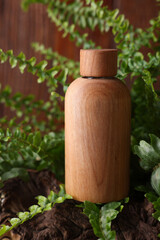 Wooden bottle of cosmetic product and green leaves on table, closeup