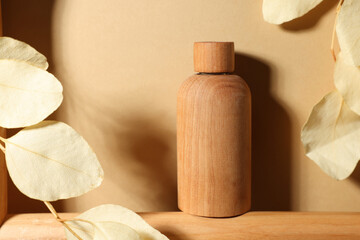 Fototapeta na wymiar Wooden bottle of cosmetic product and dried leaves on dark beige background