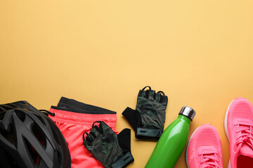 Flat lay composition with different cycling accessories and clothes on pale orange background,...