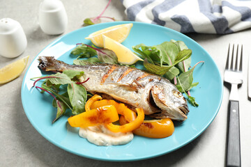 Delicious roasted fish with lemon and vegetables on grey table