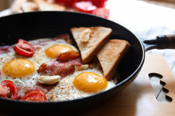 Delicious fried eggs with bacon and tomatoes in pan, closeup