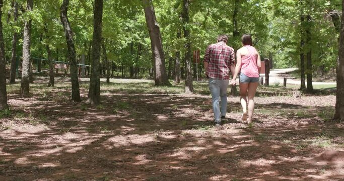 Couple hold hands while walking through the forest on their camping trip.