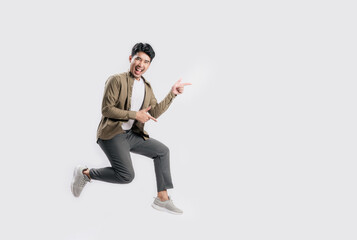 Fototapeta na wymiar Full length excited handsome young Asian man jumping in air with hand pointing to empty space on white background. Cool man joyful running in copy space. Studio short.