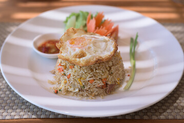 Close-up shot of Thai fried rice with fried egg served with fish sauce and vegetables, on the table.