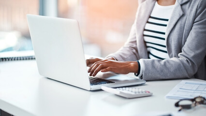 Female accountant typing on a laptop in her office or doing research on the internet while sitting at a desk. Closeup of a financial advisor working on a project or business proposal at her workplace