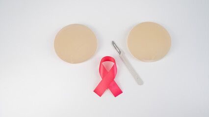 Breast silicone implants, pink tape and a disposable scalpel on a white background. 