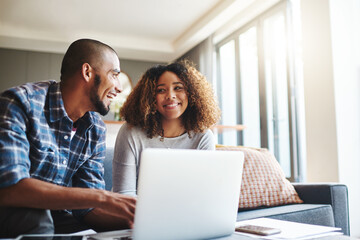 Happy, excited and cheerful couple browsing on laptop and using the internet for payments and calculating home budget while sitting on sofa. Young husband and wife enjoying convenient online banking
