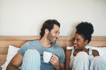 Happy young interracial couple having a cup of coffee on a bed in the morning at home. Romantic...