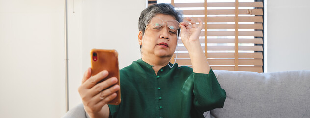 Mature asian woman have eyesight focus problem during reading text in mobile phone. - obrazy, fototapety, plakaty