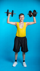 thin athlete in a yellow t-shirt and black shorts on a blue background. funny shakes muscles, goes in for sports, fitness