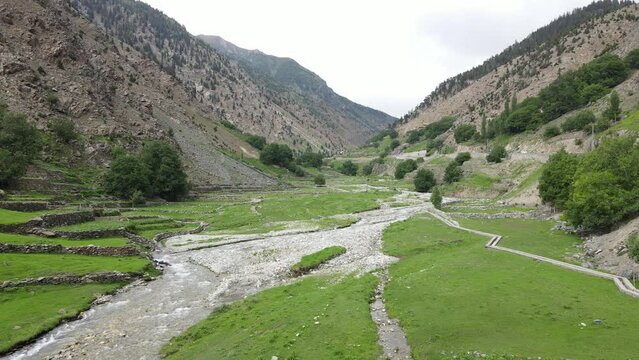 Drone flying towards a mountainous valley over a water stream, originating from the mountains of Gilgit Baltistan, Pakistan. 