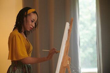 Creative Black woman enjoying painting picture on easel at home
