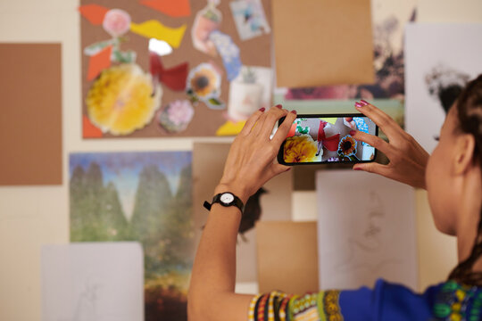 Cropped image of woman photographing collage she made to post on social media or in her online shop