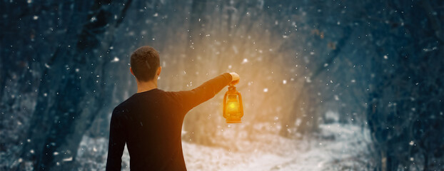 A man with a kerosene lamp in his hand walks through a snowy forest at night, a photo banner with a...