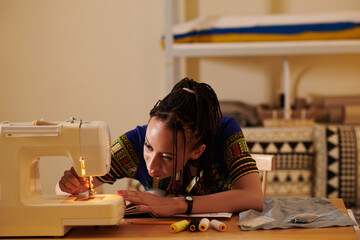 Seamstress threading sewing machine needle when working in her studio