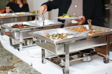 A view of several chafer dishes filled with savory entrees, seen at a local catered event. Guests...