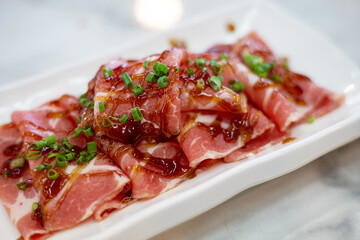 Thin slices of red pork are laid out in a ready white plate. sauces and condiments