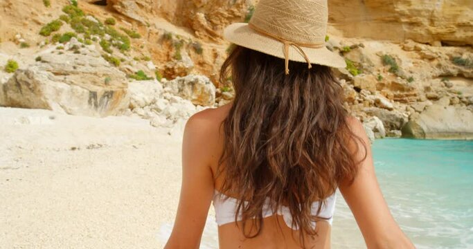 Beach, holiday and summer fun while woman with sunhat takes a relaxing and carefree walk by the ocean from the back. Young girl enjoying her vacation while walking along a sandy shoreline in summer