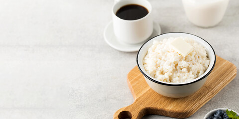 Rice porridge or pudding with a piece of butter, a mug of coffee and blueberries in a bowl. Copy space