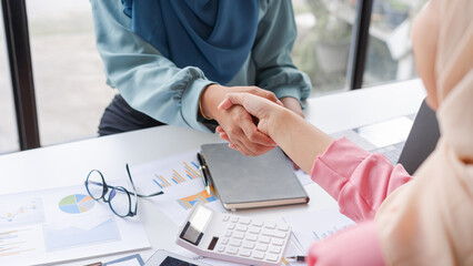 Happy Muslim female friends business woman shaking hands when working together at desk table in...