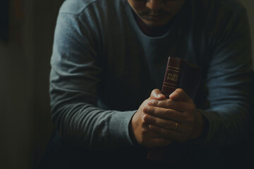 A Man praying to hold a Holy Bible. male sitting with closed eyes with the Bible in his hands,...