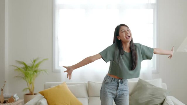 Young asian woman dancing on the floor in living room at home. Happy asia female smile relaxing in house, healthy mental wellness and wellbeing