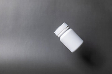White plastic pill bottle, unlabelled, capped, floating on a black background.