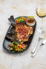 fried fish cut on a plate with salad and sauce on a white background with a glass of wine
