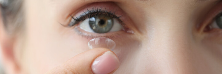 A woman inserts a contact lens into her eye, close-up