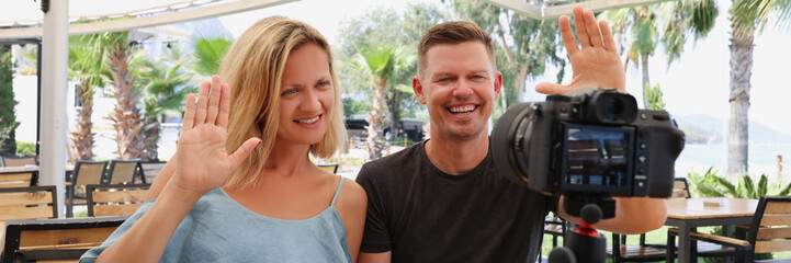 Fototapeta premium Happy couple waving at the camera on a tripod in a cafe