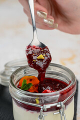 panna cotta with jam decorated with a flower in a transparent jar with a spoon
