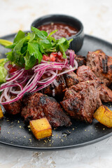 fried shish kebab in a plate with salad greens and potatoes on a white background
