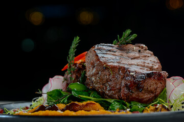 grilled meat steak on a black plate with salad and sauce on a dark background macro photo
