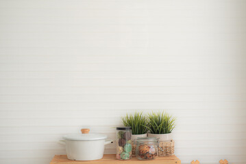Contemporary white kitchen background minimal style with white pots, a jar of cookies, a jar of dried quince sheets and a potted plant on a wooden table.