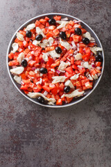 Catalan codfish salad as known as esqueixada, with cod, tomato onion and olive close-up in a plate on the table. Vertical top view from above