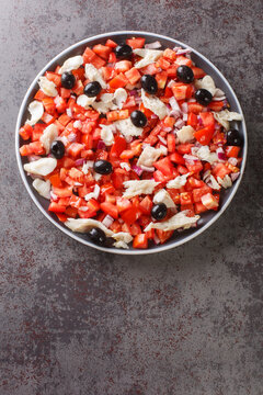 Catalan codfish salad as known as esqueixada, with cod, tomato onion and olive close-up in a plate on the table. Vertical top view from above