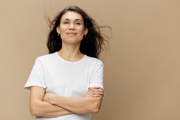 a beautiful, happy woman standing on a beige background with her hair developing in the wind, stands with eyes closed with her arms crossed on her chest