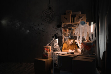 Small business dropshipping. A young businesswoman at the workplace in a witch costume sits in a warehouse at home takes an order on the site using a smartphone. big Halloween sale concept.