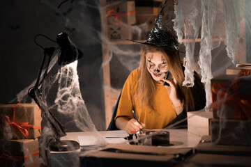 Small business dropshipping. A young businesswoman in a witch costume is sitting in a warehouse taking an order about by phone. Big Sale on Halloween.
